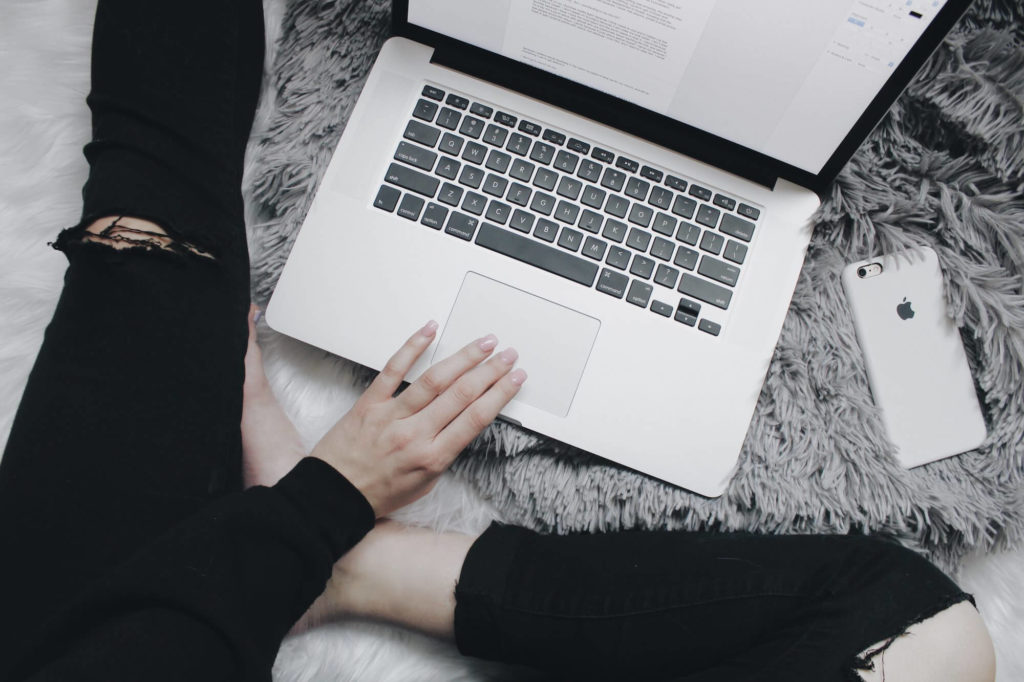 girl with laptop in lap next to iphone working to drive more traffic to her blog