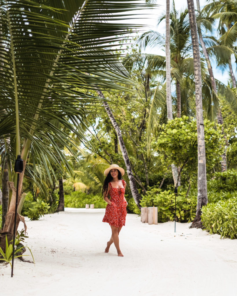 Isabella in a red dress walking under palm trees on the sand in The Maldives 