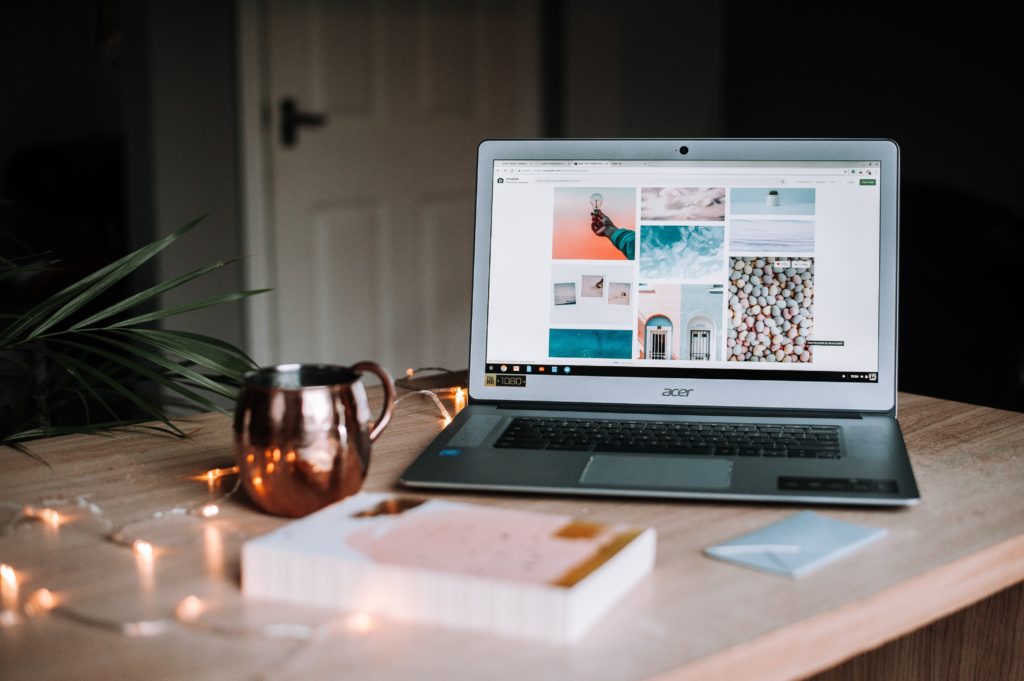 An acer laptop, metallic cup and book on a desk with fairy lights 