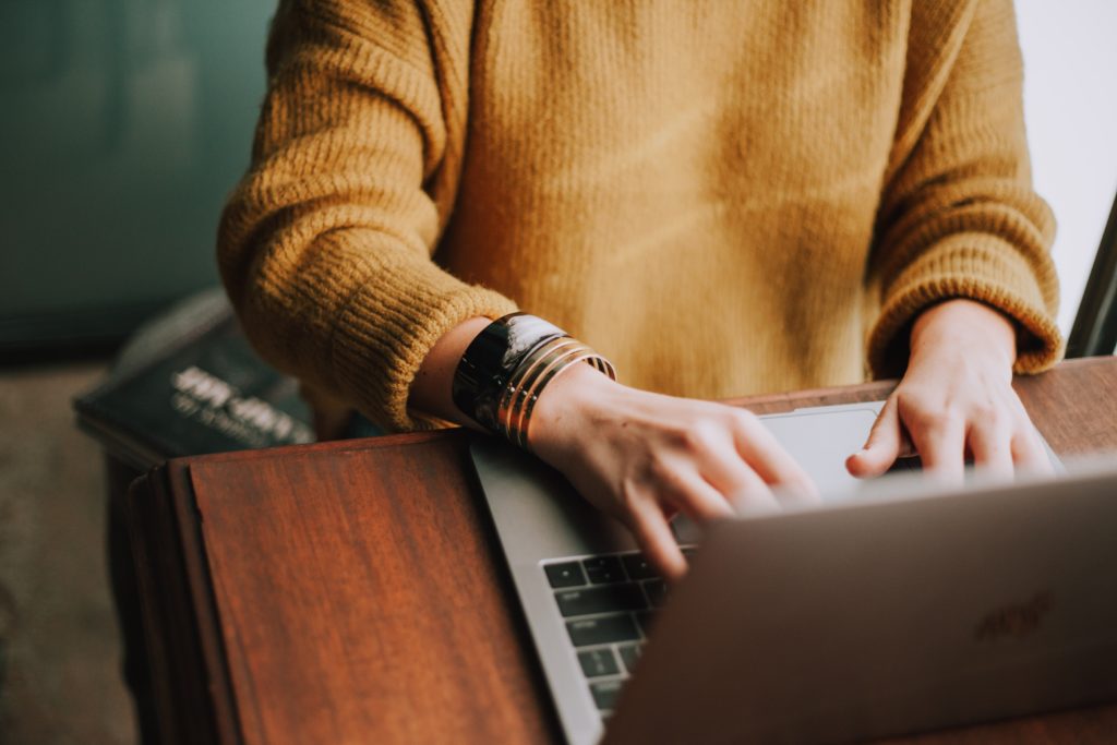 Woman in yellow jumper typing on a laptop 