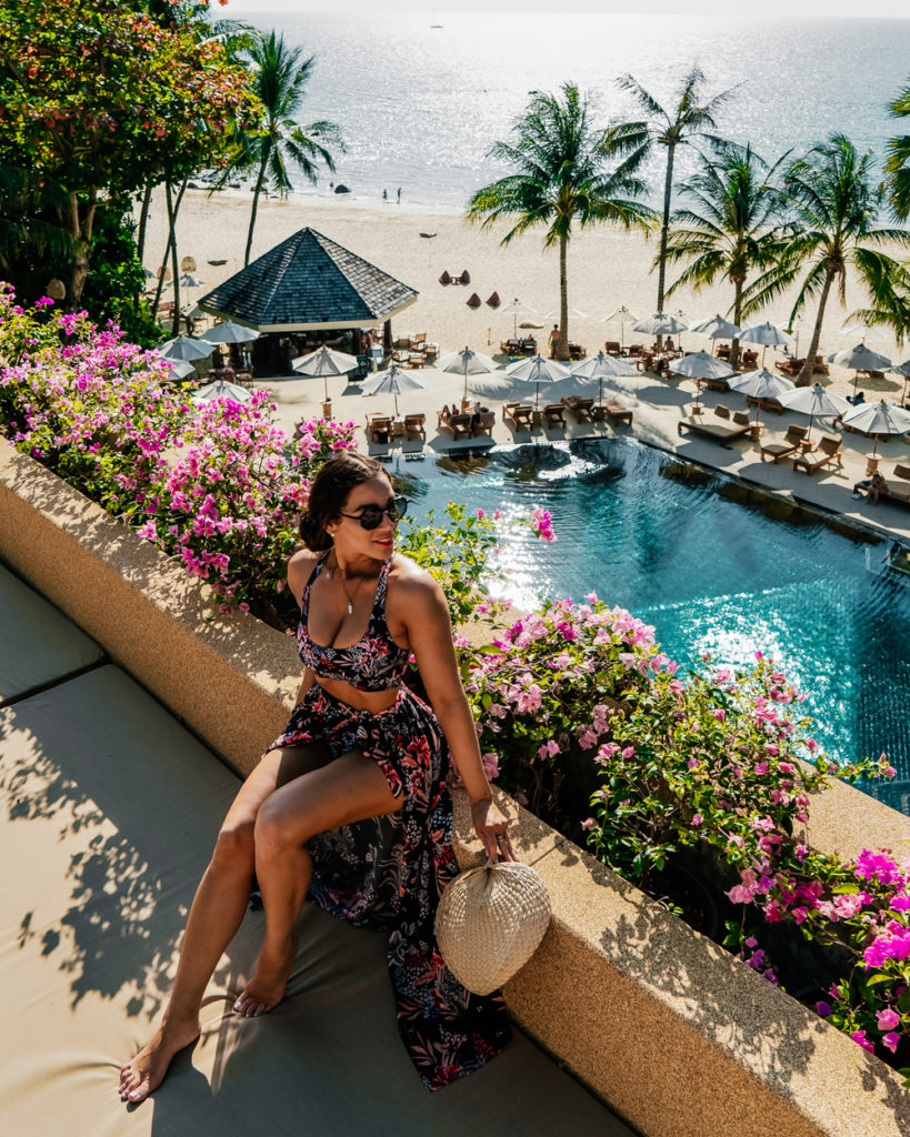 Isabella sitting on a wall overlooking a swimming pool and beach in Thailand 