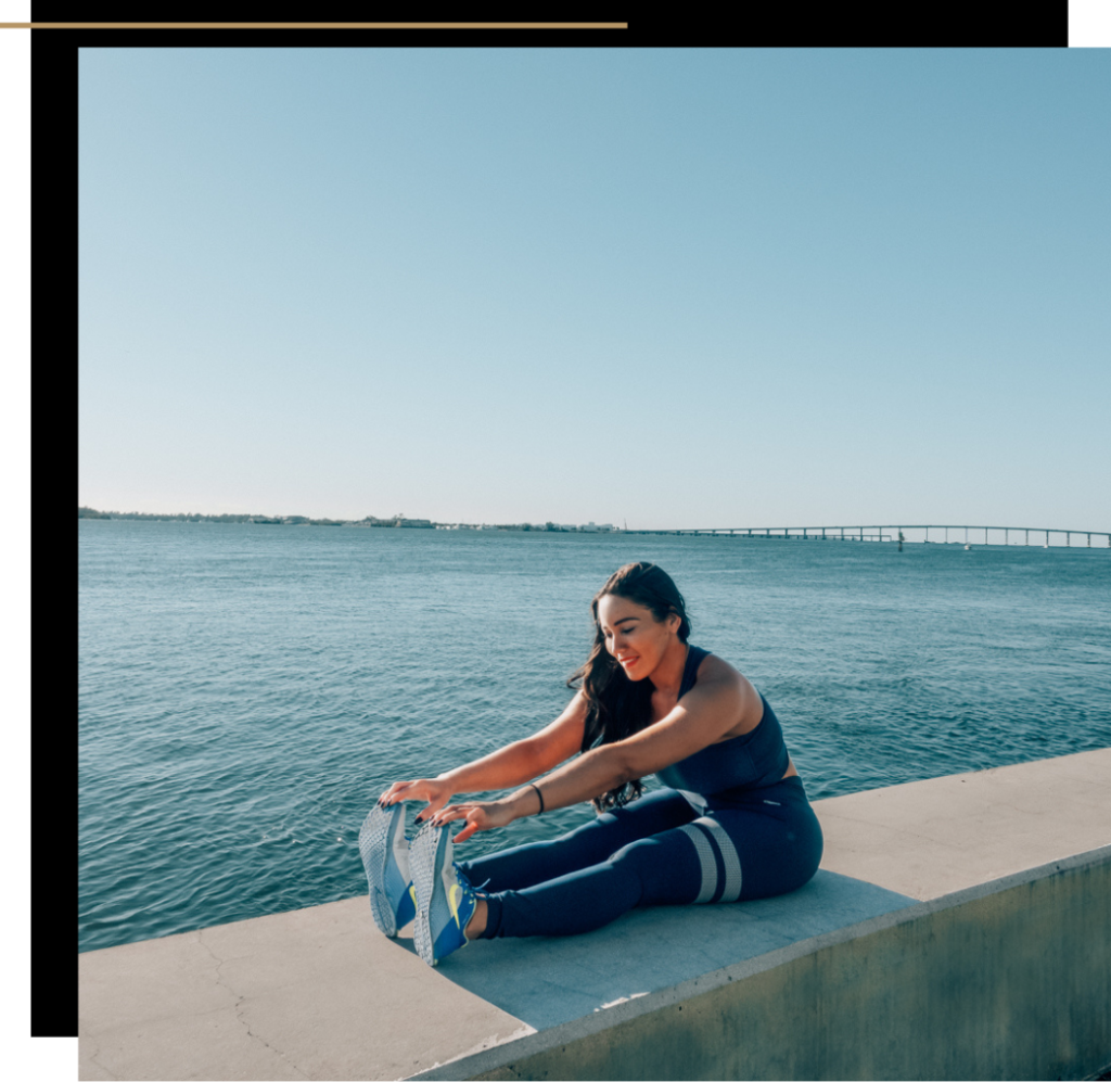 Isabella in activewear stretching on a wall by the water 