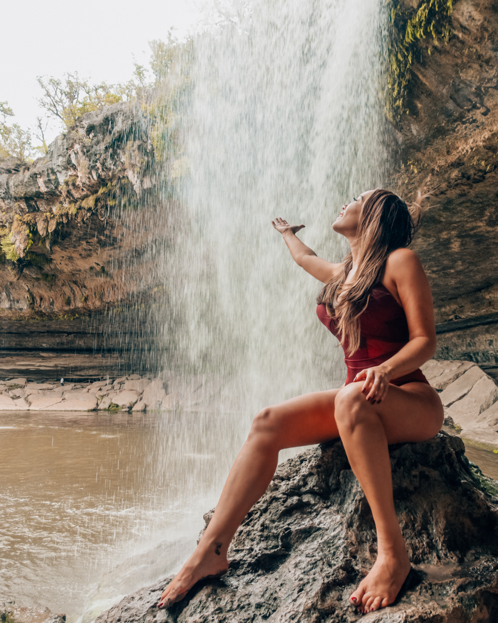 Isabella in a red swimsuit sitting on the rocks of the Hamilton Pool in Austin, TX